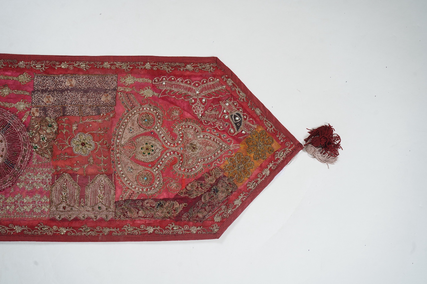 An Indian 20th century red silk marriage banner/hanging, ornately embroidered in silver and gold thread, with raised stump work flowers, corded and designed using simulated pearls and coloured beads etc., 74cm x 43cm. Co